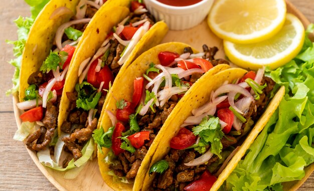 A plate of authentic beef tacos topped with fresh cilantro, lime wedges, and avocado slices.