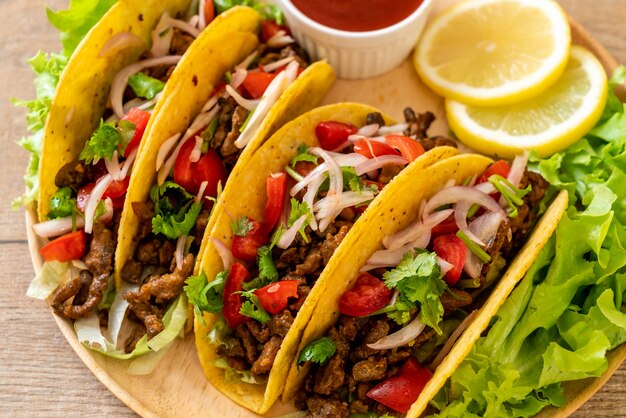 A plate of authentic beef tacos topped with fresh cilantro, lime wedges, and avocado slices.